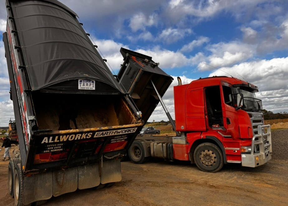 Red tipper truck lifting its tray to dump soil on-site.