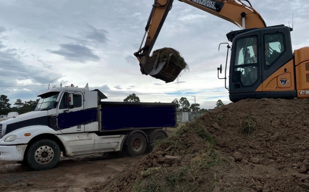 Excavator placing soil into a truck during earthmoving.
