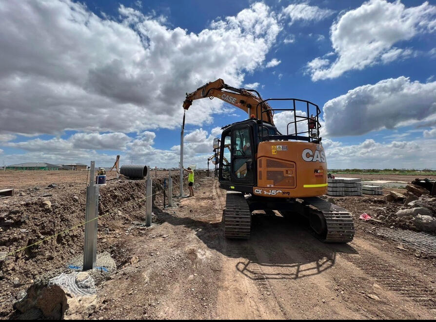 Case excavator digging and levelling earth on a large open site.